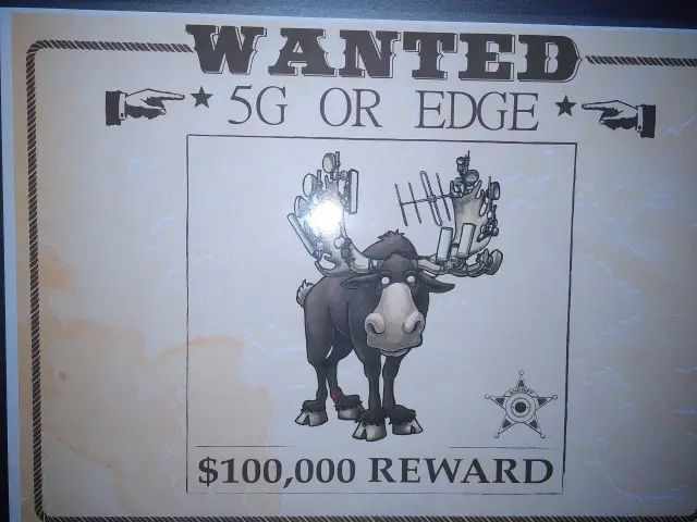Ein Papieraushang. Er ist im Stil eines Wildwest-Wanted-Posters. Oben steht „WANTED 5G OR EDGE“, darunter ist ein Bild des Datenelches und darunter der Text „$100,000 REWARD“.